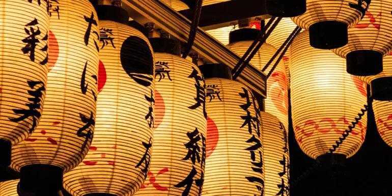 a dozen white lanterns with red and black designs and script hanging side by side