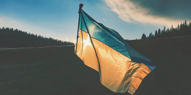 Ukraine flag with blue sky, hills and trees in the background