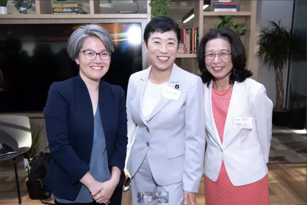 Three women all wearing blazers standing in front of a TV in a room