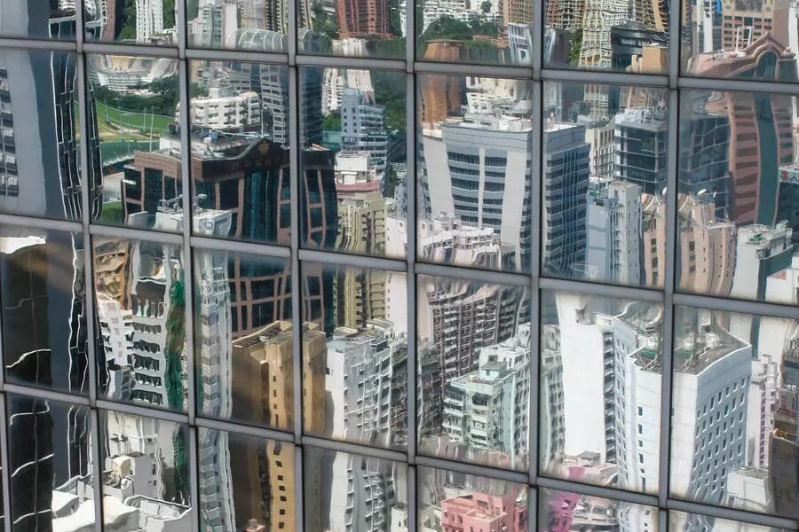 A glass mirrored building facade reflects a distorted image of more high rise buildings.