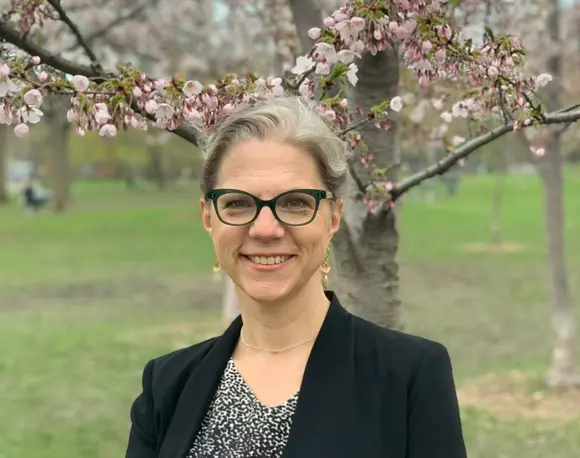 Picture of Pamela Klassen standing in front of a cherry blossom tree wearing a black blazer. 
