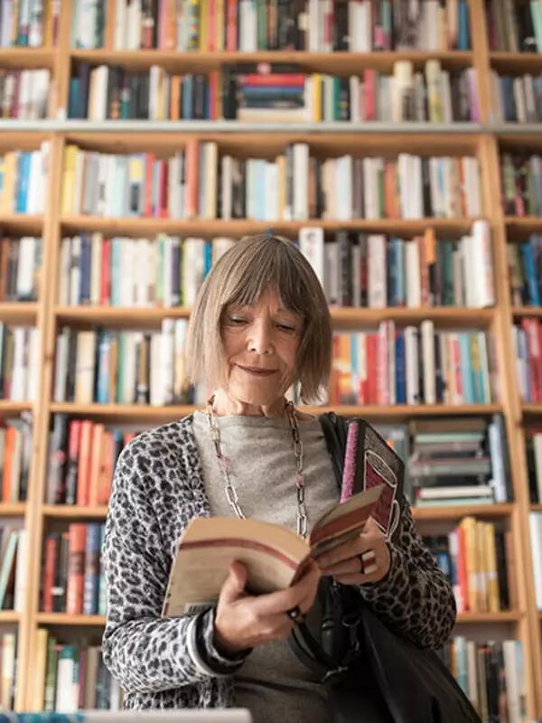 Ksenya Kiebuzinski stands reading a book in front of a wall of bookshelves