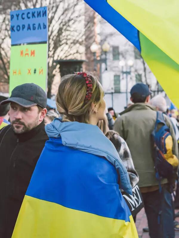 A woman wearing a Ukrainian flag stands at an anti-war protest.