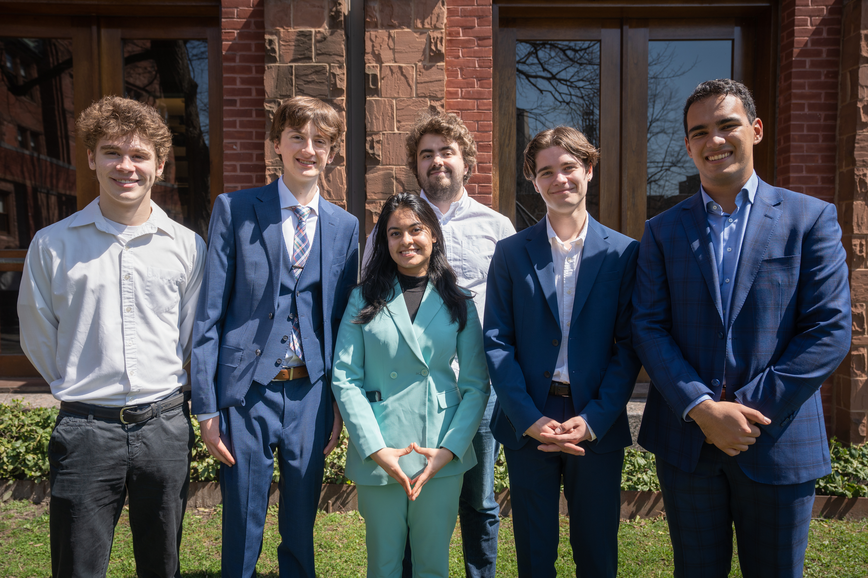 Six students wearing business attire smile in the Munk garden in 1 Devonshire Place