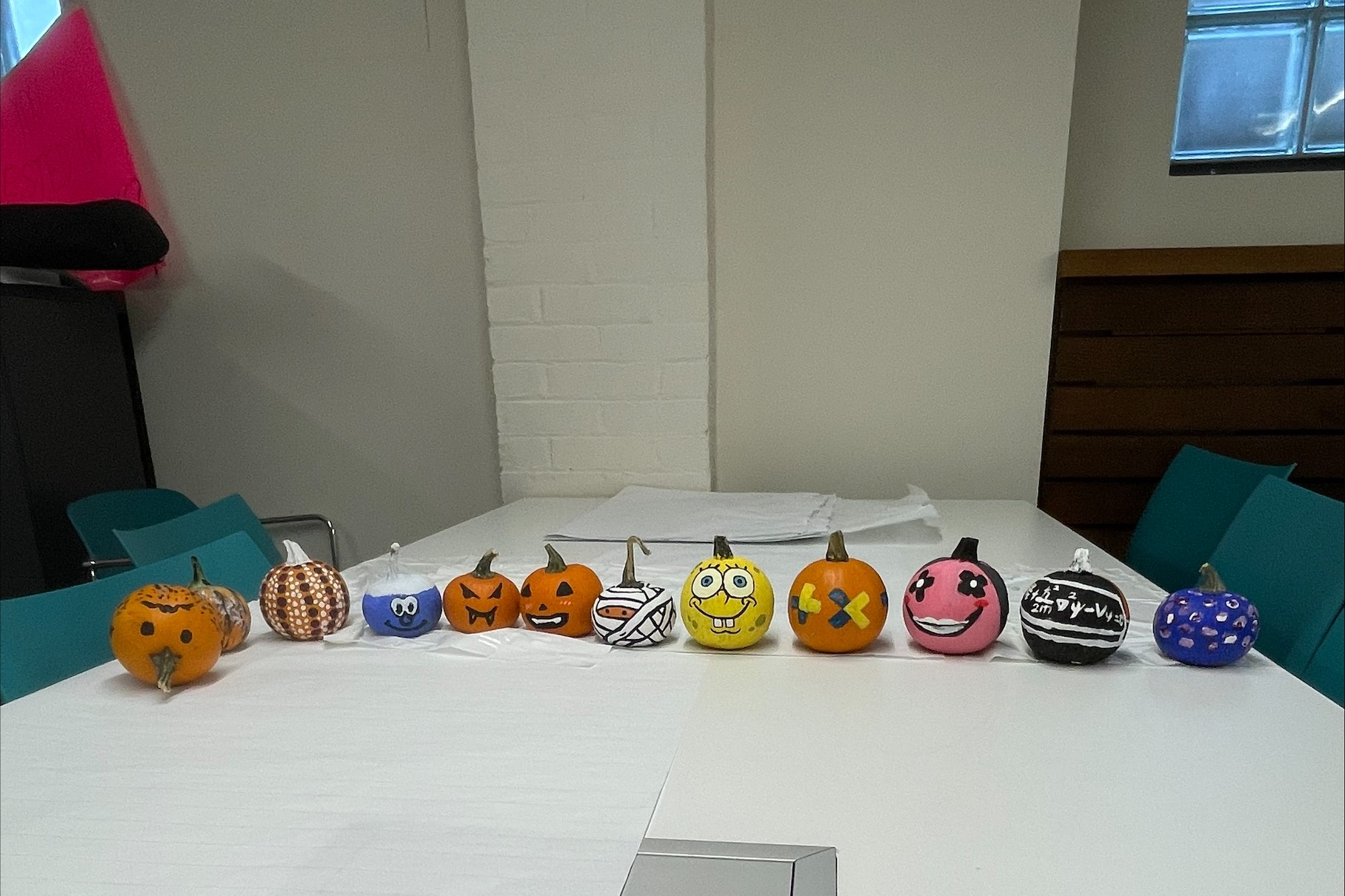 A series of colourful painted pumpkins are lined up on a white table. 