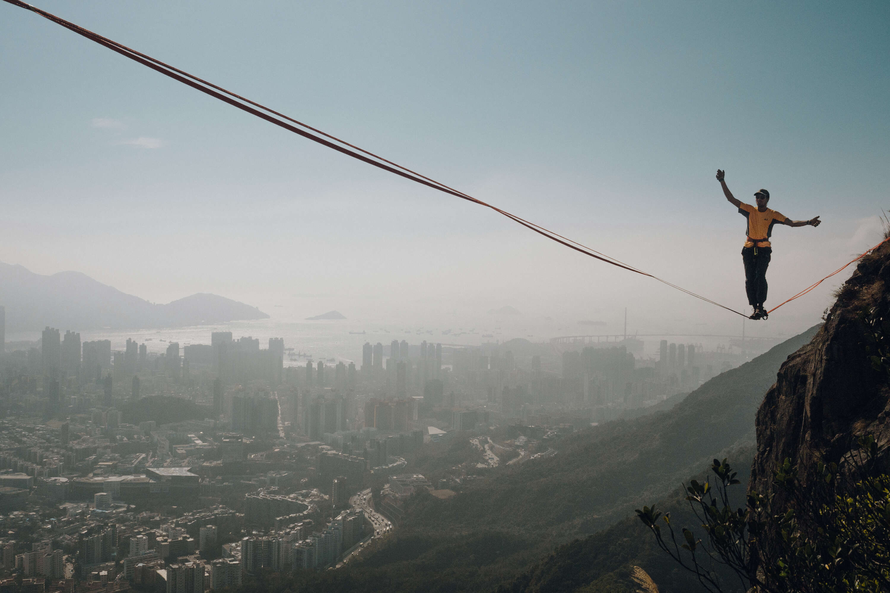 Photo of a man tightrope walking over mountains with a view on Hong Kong. 