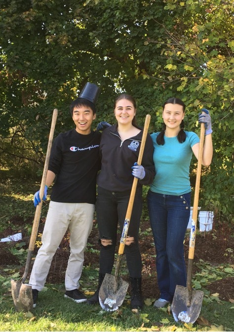 Three Munk One students smiling with shovels while planting trees in the Toronto Park.