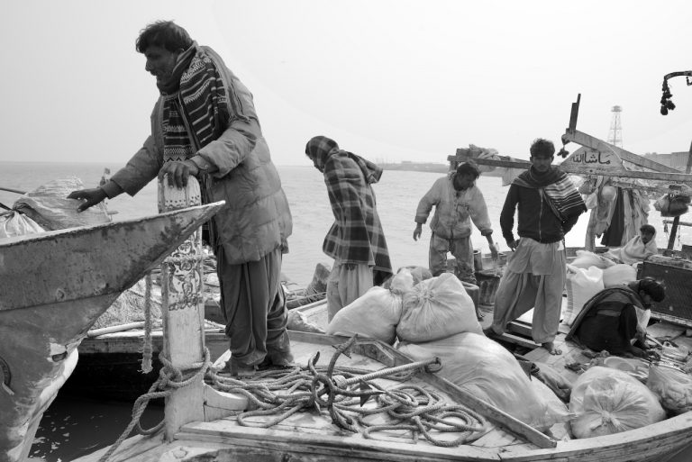 A black and white photo of a group of men fishing in a small boat.