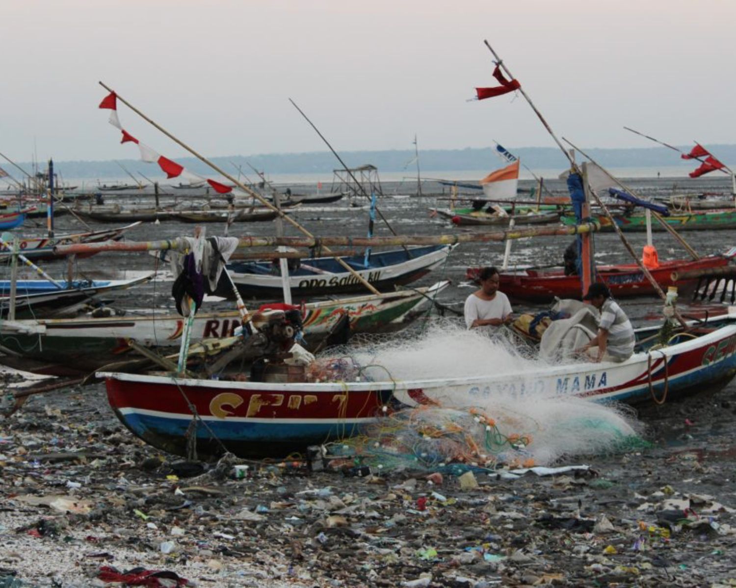 Fishermen removing debris from fishing nets at Kenjeran Beach, Indonesia