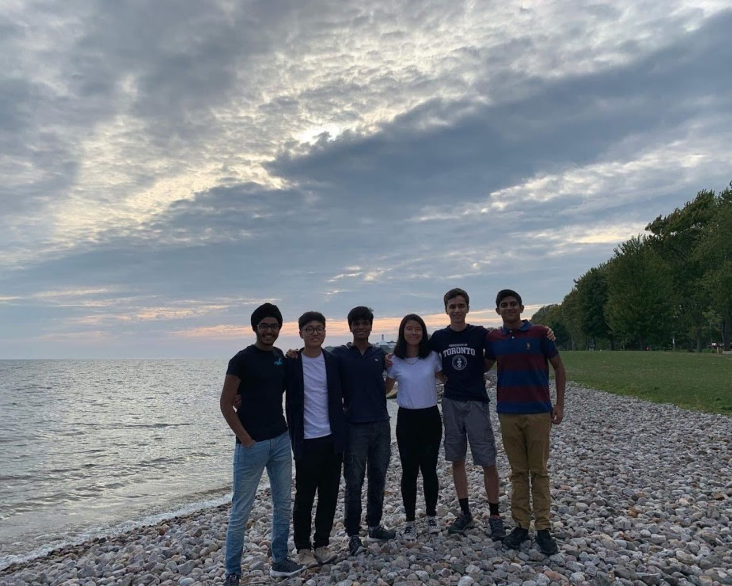 A group of smiling students standing outside on a rocky beach.