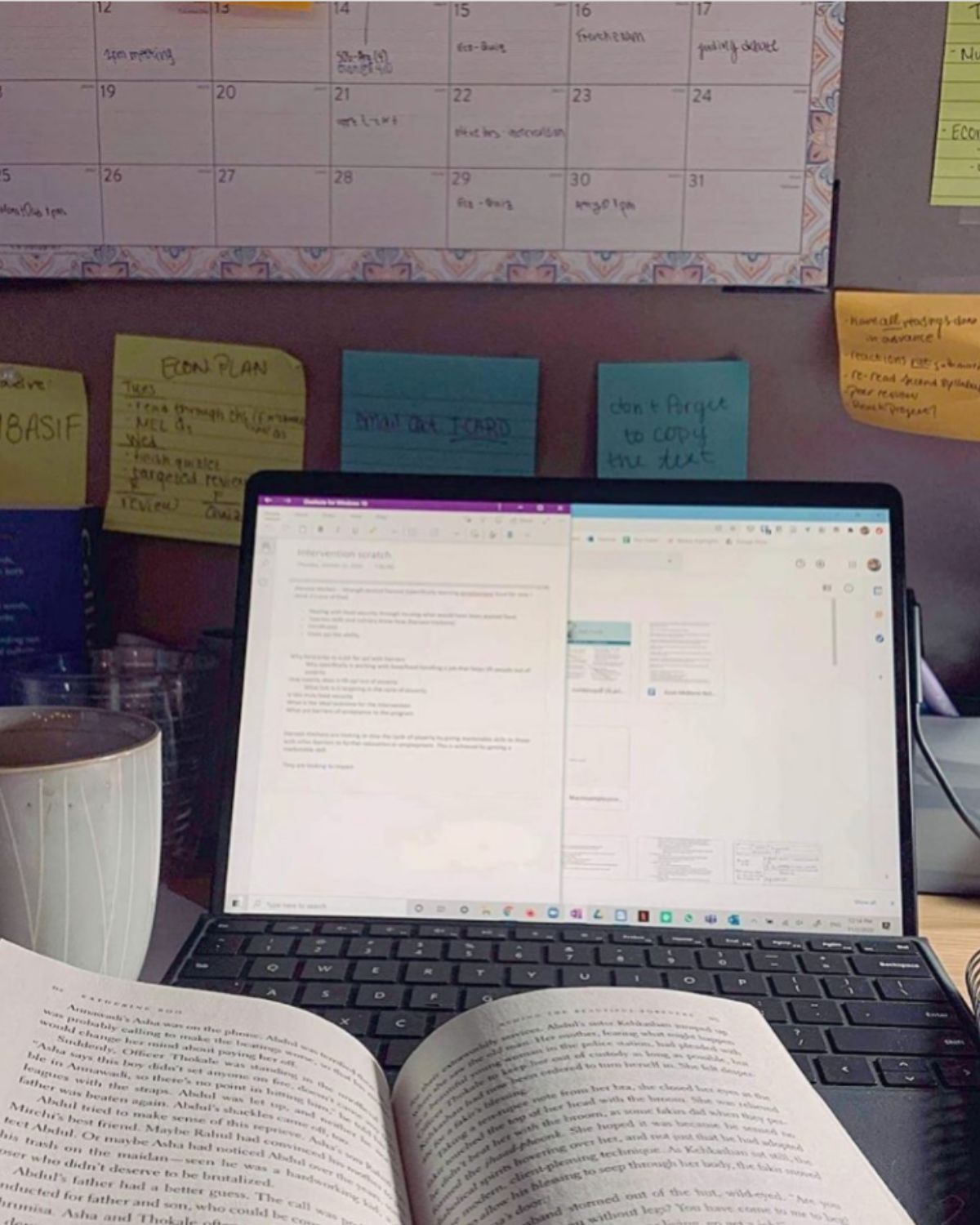 A laptop and a calendar behind a textbook on a desk.