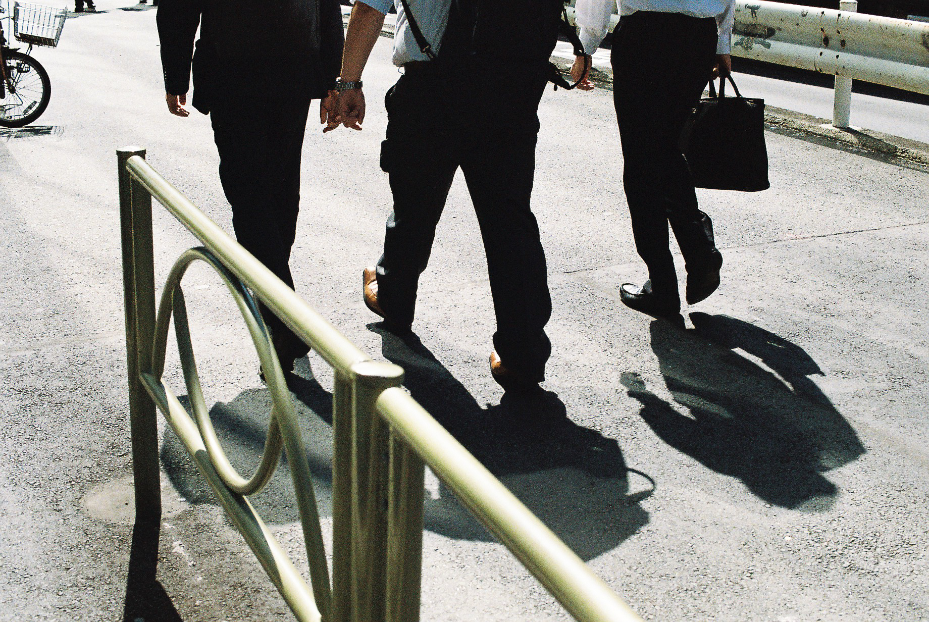Photo of three men dressed for work walking on a street, with only their legs in the shot. 