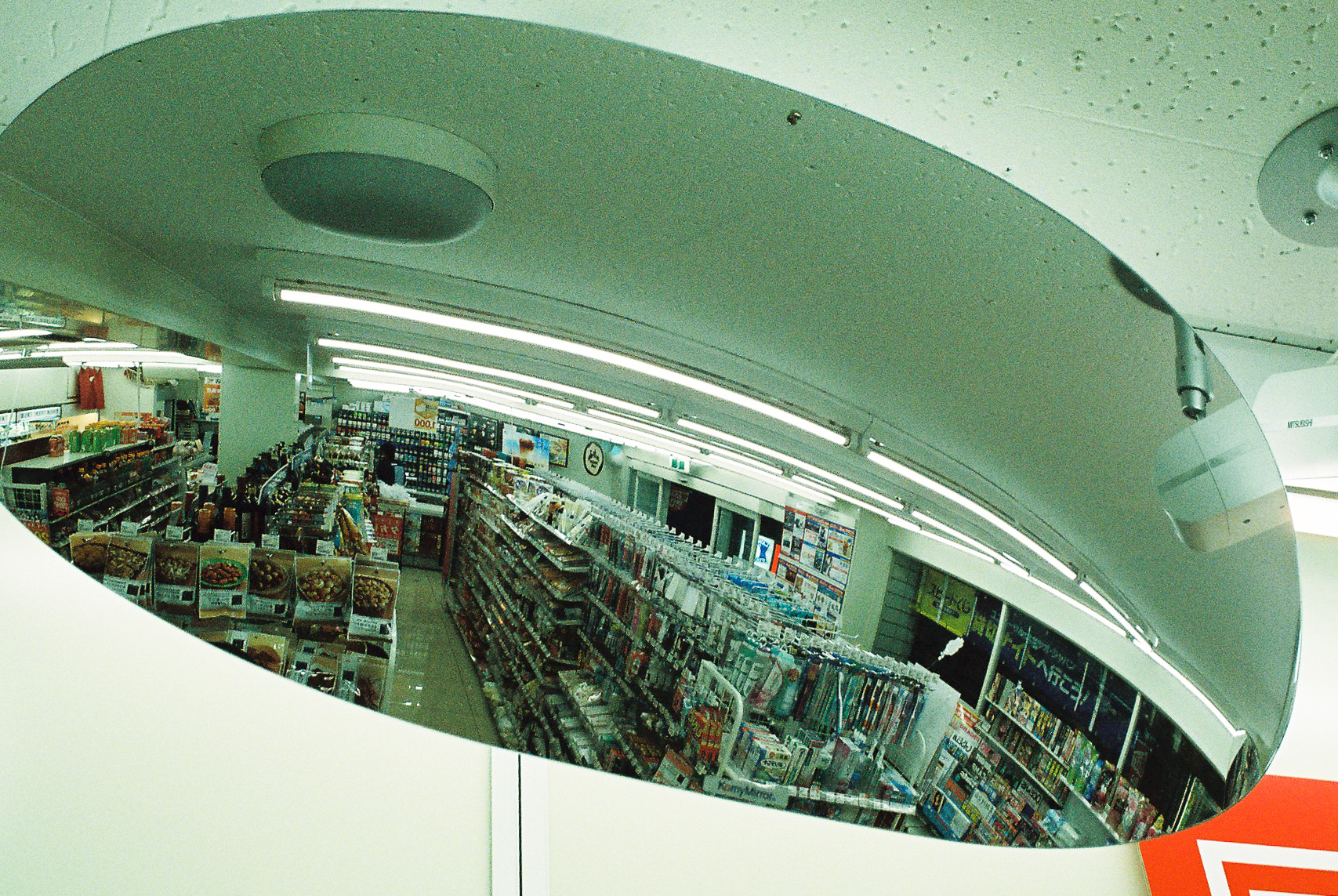 Photo of the shelves in a convenience store reflected in a convex security mirror. 