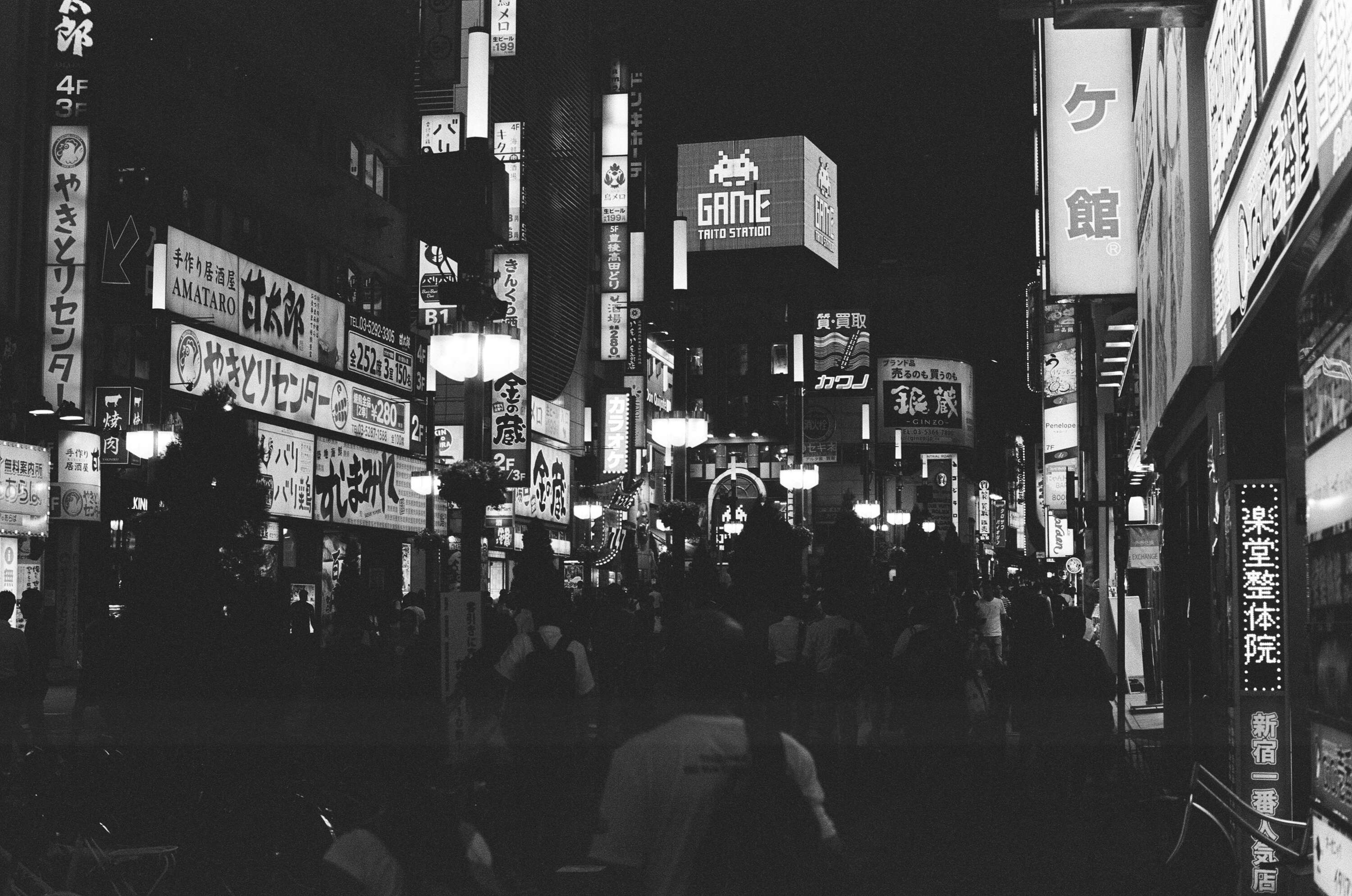 Black and white photo of a crowded street in Tokyo with neon billboards lighting up the street.