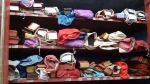 Three shelves filled with manuscripts wrapped in colored fabric