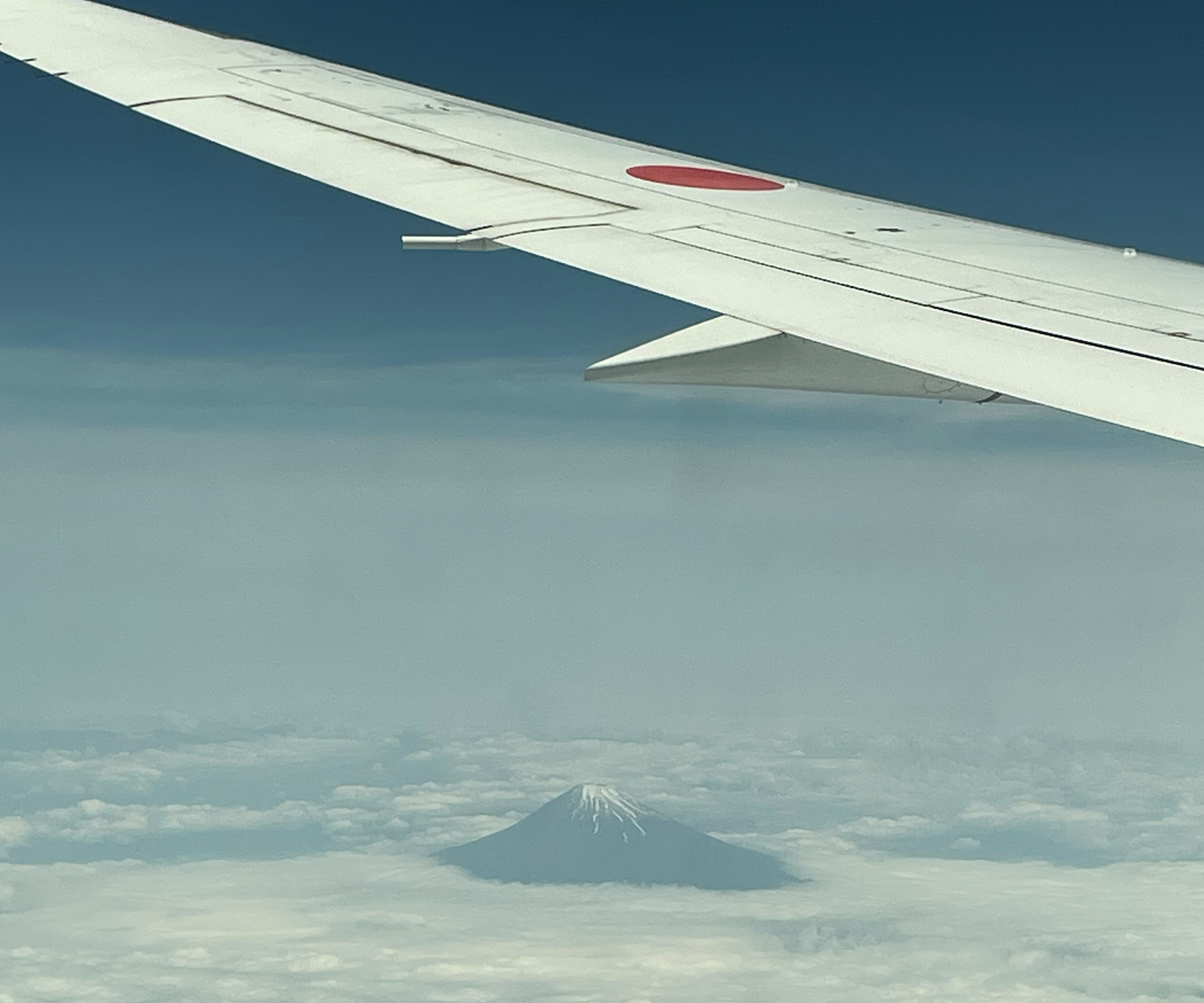 View of airplane wing over clouds with top of Mount Fuji peaking up through the clouds