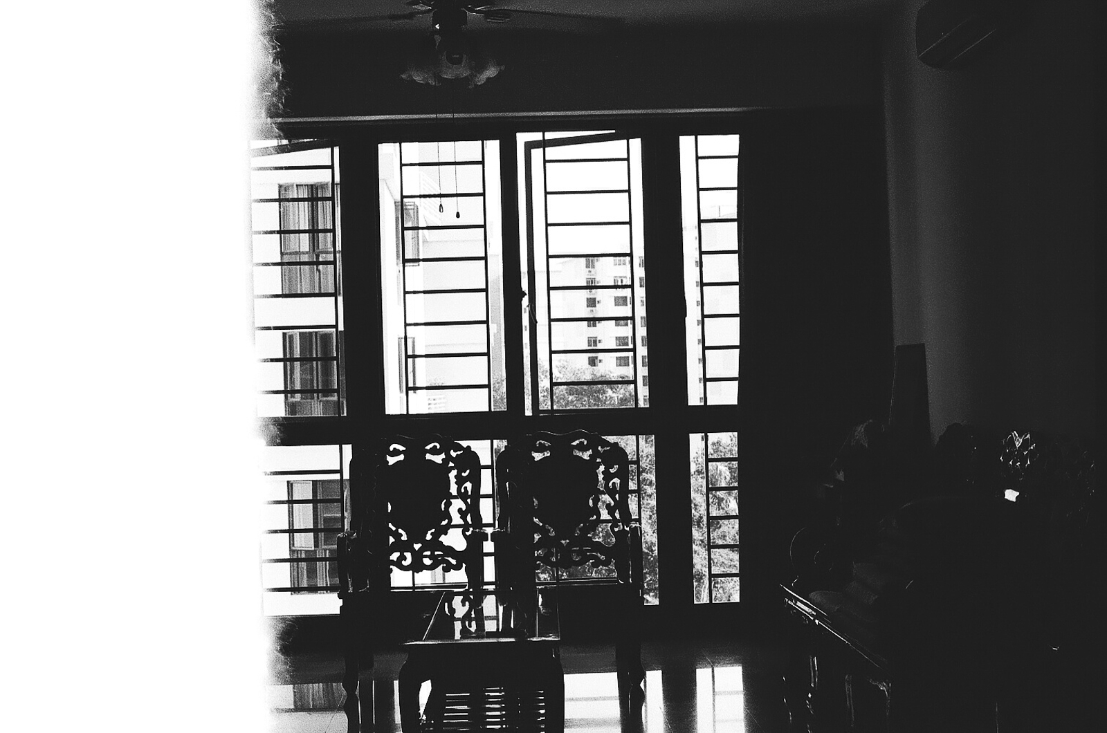Black and white photo of a room with two chairs placed in front of a window. The left side of the photo is blurred with white color.