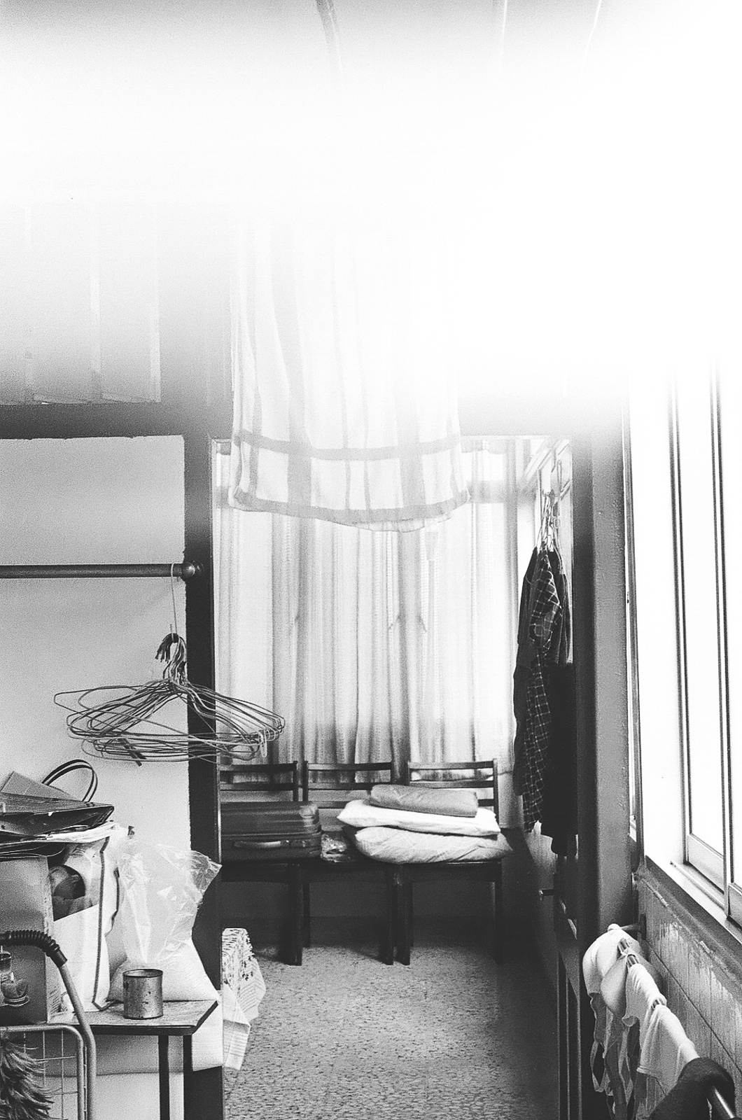 Black and white photo of a room cluttered with furniture and clothes hangers on the door handle.