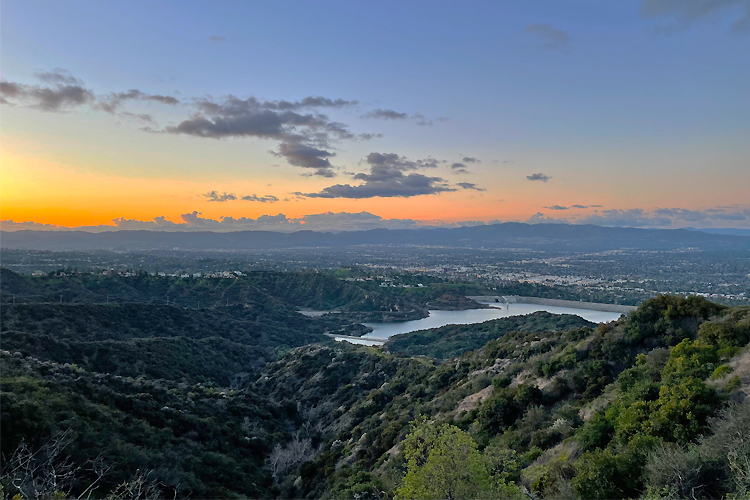 A scenic image of mountains and lakes in between with a sunset in the back.