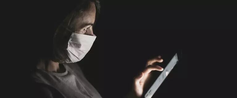 A masked woman swipes on her phone in the dark