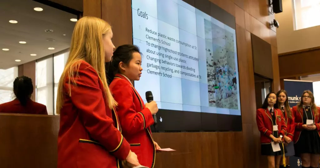 Three GII participants stand beside a presentation screen in red school uniforms 