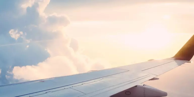 The wing of an airplane with sun and clouds on the horizon