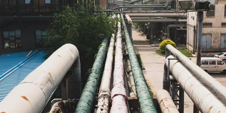 Several large pipes running through a city with buildings in the background
