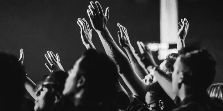 Black and white photo of a small crowd of people with their hands up in the air
