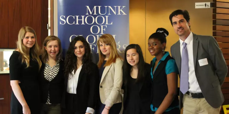 Group of six students and a teacher in front of a Munk School banner