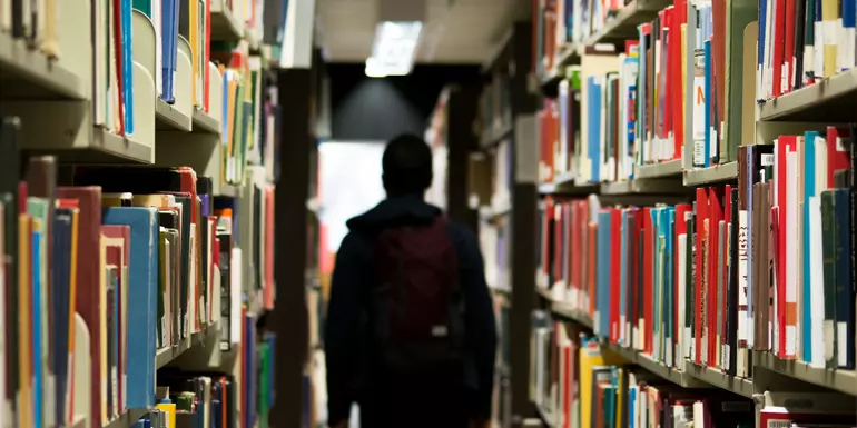 Person walks between two shelves of books in a library