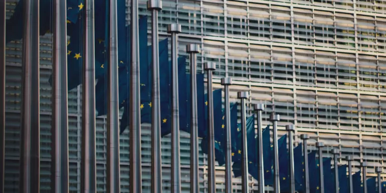 A long row of flagpoles with EU flags in front of a building