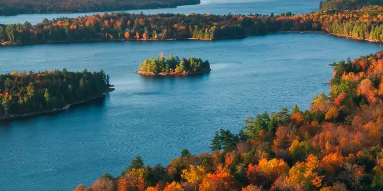 Arial photo of a lake with two islands, surrounded by trees with autumnal colours