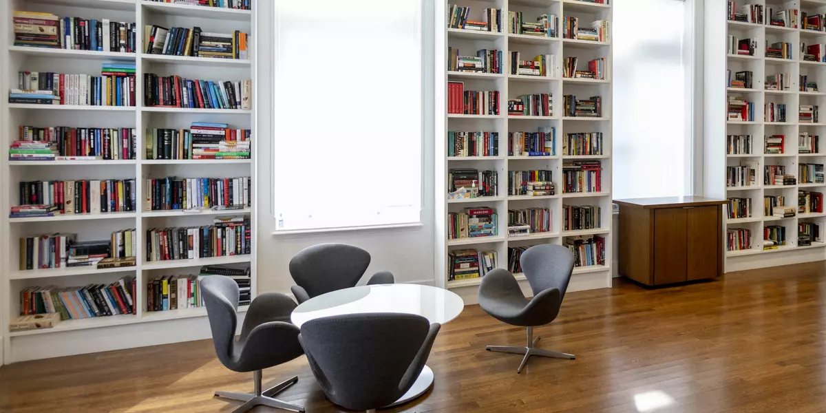 Munk School library with white bookshelves, two large windows, a round table and four grey chairs