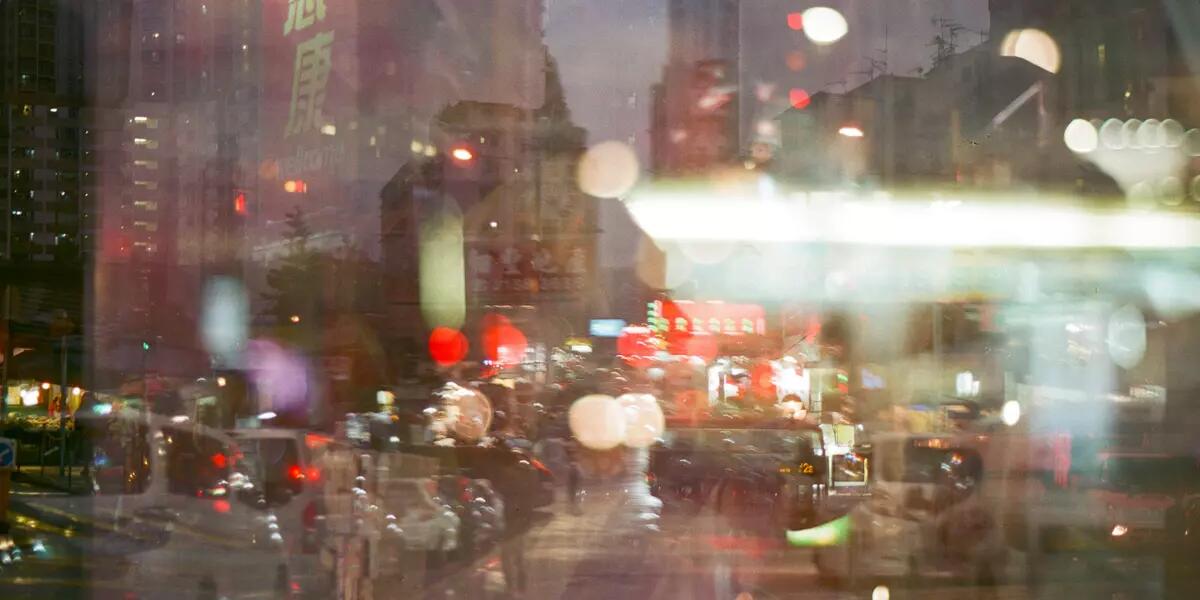 A Hong Kong street scene in the evening, with red lanterns, tall buildings in the background, and blurry lights from double exposure.