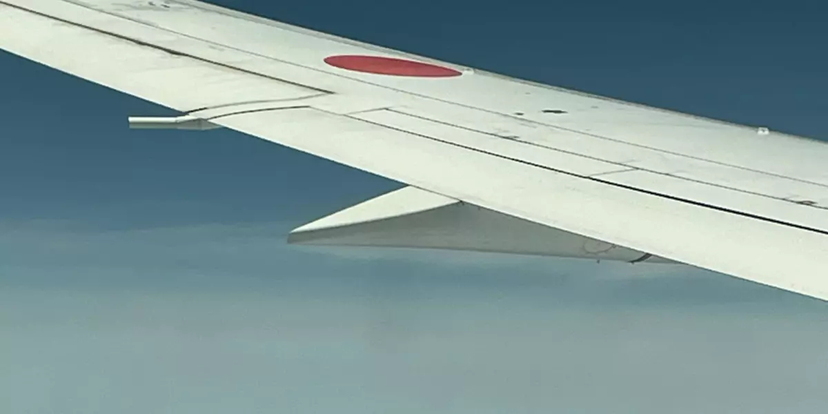 Plane wing over clouds with the top of mount fuji peaking through the clouds