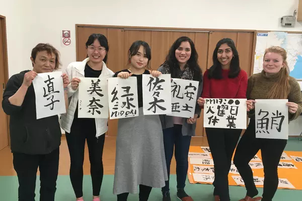 Six students each holding a piece of white paper with Japanese characters on them