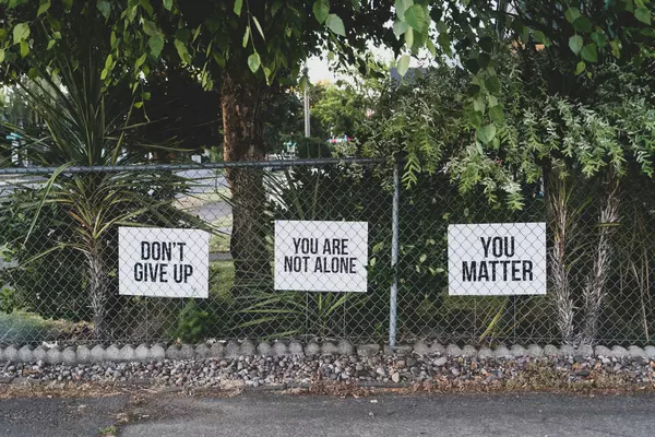 Three signs attached to a fence read don't give up, you are not alone, you matter