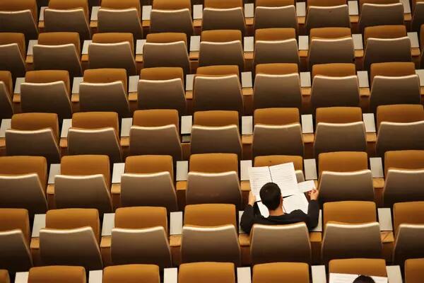 Arial photo of rows of empty auditorium chairs and the back of one person sitting and reading