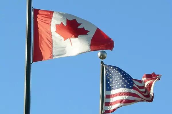 Canadian and U.S. flags on flagpoles against a blue sky