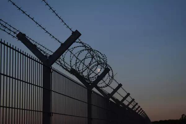 Long stretch of fence, topped with barbed wire, at dusk