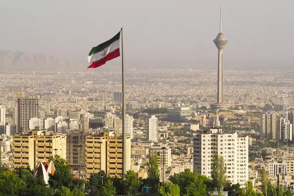 Flag of Iran flown from above, city in the background