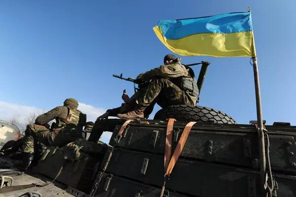 Ukrainian sitting on top of a tank bearing the flag of Ukraine