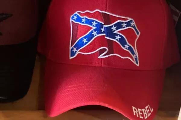 Red baseball cap bearing the confederate flag and the word "rebel." Route 6 Steel Horse Boutique in Port Dover, Ont., sells merchandise including this ball cap featuring the Confederate flag. The Oxford Caribbean Canadian Association says the symbol 'represents the fight to maintain slavery as a social and economic structure.'  on the bill. 