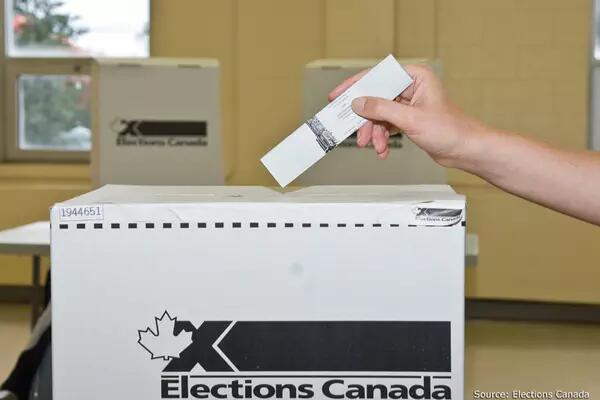 An outstretched hand puts their ballot into an Elections Canada voting box