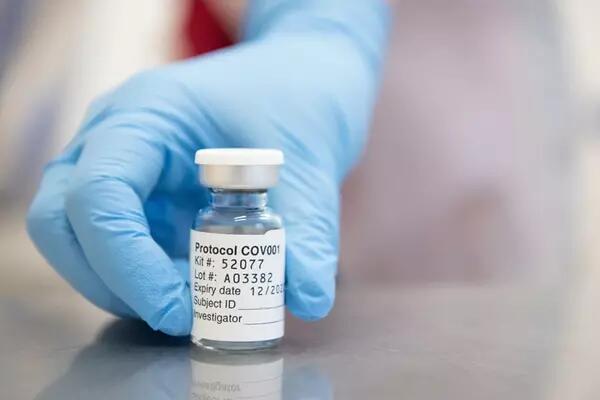 Blue gloved hand pushes forward a vial of the COVID vaccine