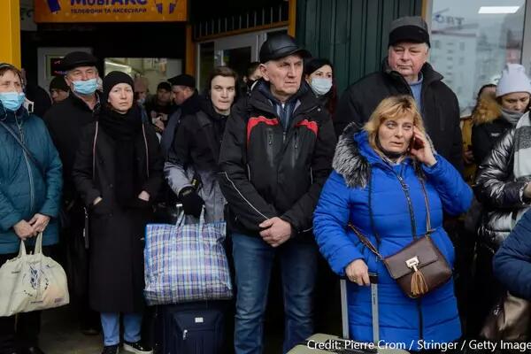 A group of Ukrainians dressed in winter coats and masks with luggage/belongings waiting, presumably for evacuation details