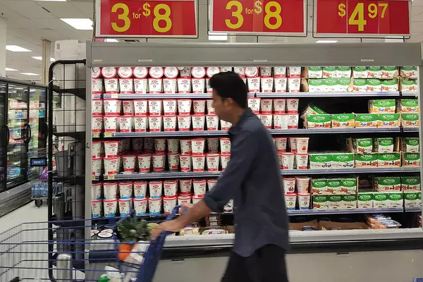 Man walks with a grocery cart down an aisle, shopping for groceries. Prices for items are in the background.