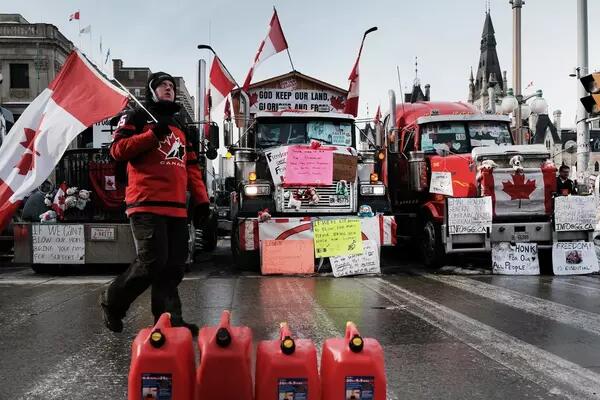  Freedom convoy blockade with trucks, signs, canadian flags, barrier made of gasoline cannisters