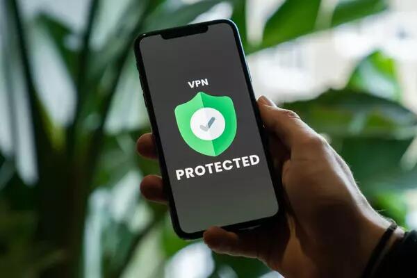 A person holding a phone in their hand. The screen has a green shield with a check mark in the middle, with "VPN" above and "PROTECTED" below the shield 