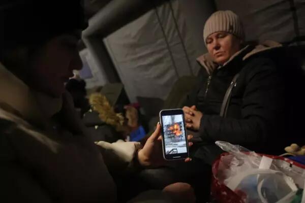 Two Ukranians look at an image of a fiery building on an iPhone screen